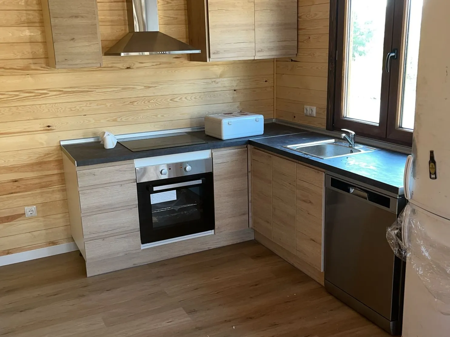 La mateixa cuina acabada, amb taulell fosc, placa, forn, aigüera i rentaplats